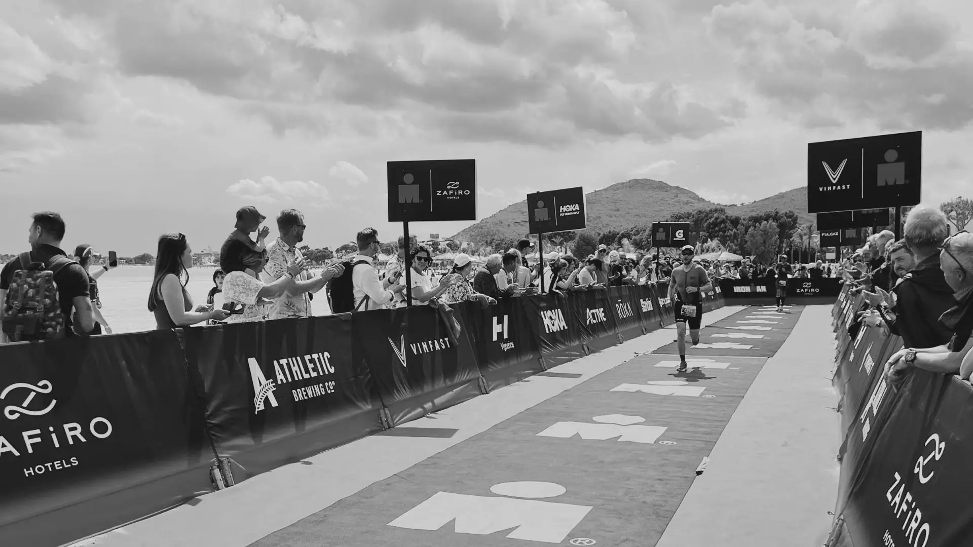 Pretekár beží cieľovou rovinkou pretekov IRONMAN pomedzi povzbudzujúcich divákov